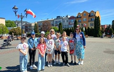 Na Placu Kościuszki w Sochaczewie grupa uczni&oacute;w na tle flagi