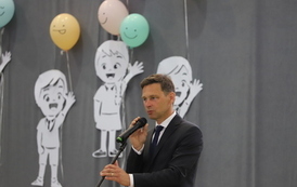 Pan Arkadiusz Karaś - wiceprzewodniczący Rady Miasta przemawia do uczni&oacute;w i rodzic&oacute;w, w tle dkoracja - postacie dzieci wycięte z papieru.