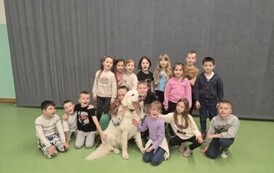 Uczniowie klasy 1b wraz z owczarkiem podhalańskim i panią Agnieszką podczas zajęć dogoterapii. 