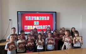 Grupa dzieci stoi na tle dekoracji z napisem &bdquo;Pasowanie na czytelnika&rdquo;. Dzieci trzymają w rękach książki.