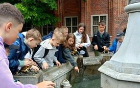 Uczniowie stoją koło fontanny i patrzą co znajduje się w niej